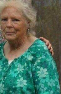 Elderly woman in green floral blouse, outdoor setting, representing compassionate pet memorial services.
