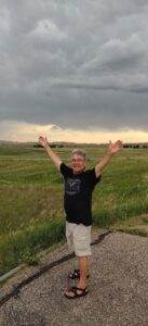 A peaceful man standing in a grassy field with arms outstretched under a cloudy sky.