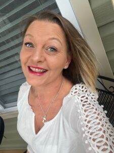 Gentlewoman smiling outdoors in white lace top, emphasizing compassion and care.