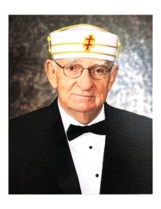 Veteran in formal attire with ceremonial cap, Tennessee flag, and glasses, honoring military service.