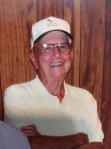 Gentleman wearing a white cap and glasses, smiling warmly in front of a wooden wall.