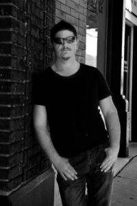Relaxed man wearing sunglasses standing outside brick building.