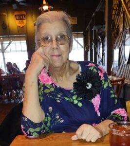 Comfortable elderly woman in floral blouse sitting at a restaurant table, smiling.