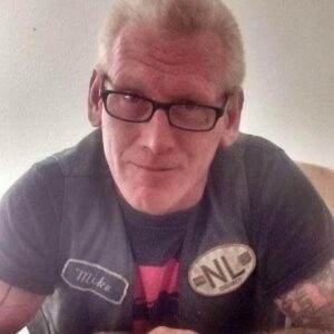 Friendly man with glasses and tattoos, smiling in casual attire.