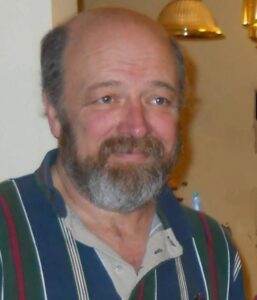 Gentleman with a beard smiling indoors, warm atmosphere, supportive cremation services.