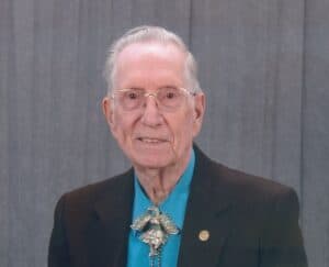 Aging man with glasses wearing a bolo tie and blazer, portrait headshot, professional, respectful.
